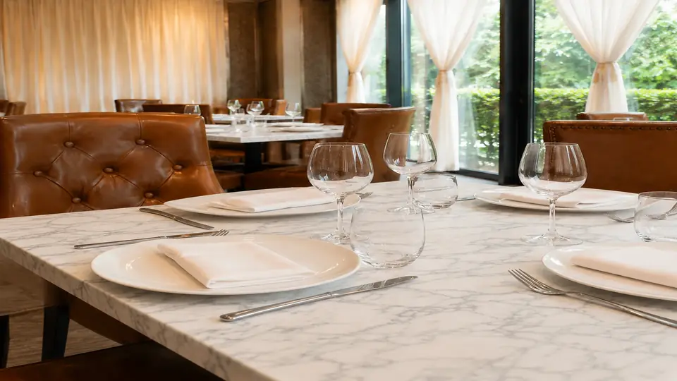 Close view of a marble tabletop at CALI Raffles Place, set with white china, folded napkins and glassware.